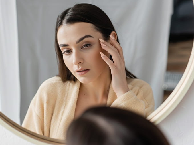 肌に悩みながら鏡で自分を見る女性のイメージ写真